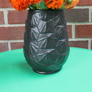 May include: A black geometric vase with a textured surface, filled with orange flowers.
