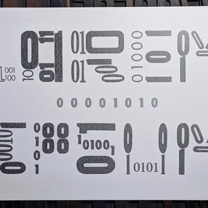 May include: A print on white paper featuring a series of grey numbers and binary code elements. The design includes various sizes and styles of the numbers 0 and 1, arranged in a seemingly random pattern, with the binary code "00001010" in the centre.