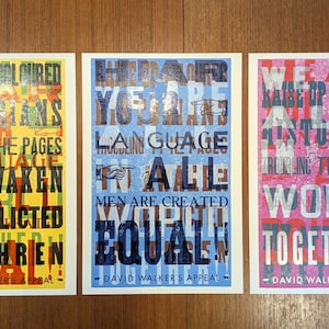 May include: Three rectangular art prints featuring layered typography. The left print has a yellow background with black text. The center print has a light blue background with dark blue text. The right print has a pink background with white text.