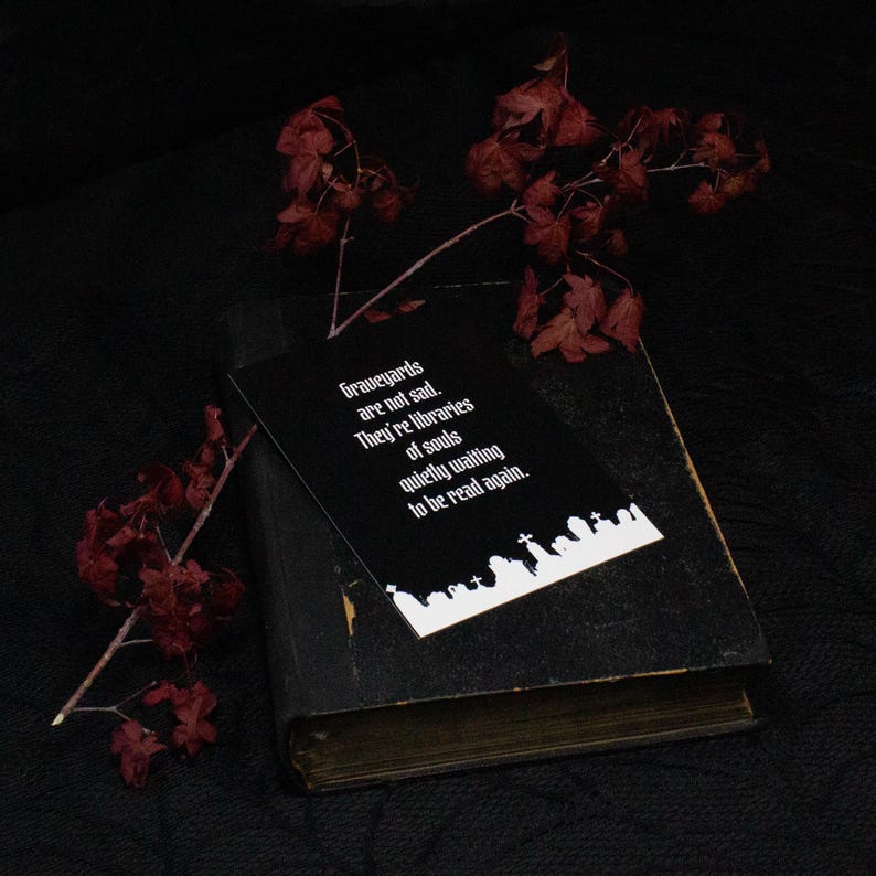 以下が含まれることがあります： 「Graveyards are not sad. They're libraries of souls quietly waiting to be read again.」という白い文字が書かれた黒い長方形のカード。テキストの下には白い墓地のシルエットがある。カードは使い古された黒い本の上に置かれている。