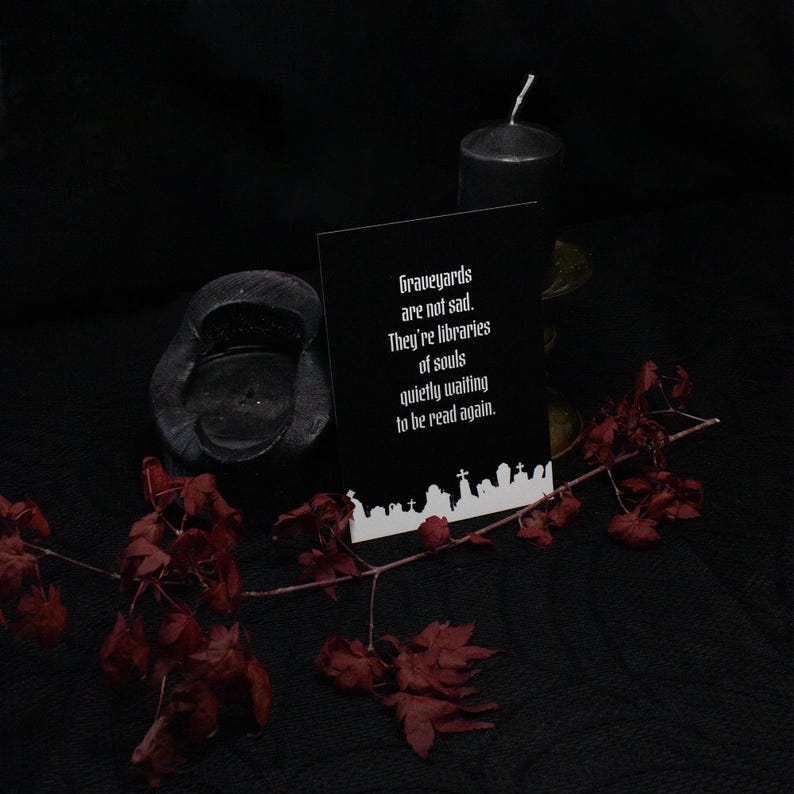 以下が含まれることがあります： 「Graveyards are not sad. They're libraries of souls quietly waiting to be read again.」という白い文字が書かれた黒い長方形のカード。カードの下部には、墓石や十字架が並ぶ墓地の白いシルエットが描かれています。