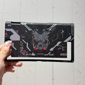 May include: A black protective console case featuring a mechanical skull graphic with red accents, geometric patterns, and white text including "PRODUCE" and "SWITCH". The design incorporates technical lines and symbols across the surface.