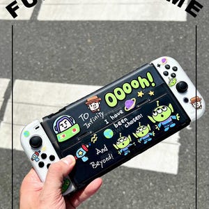 Puede incluir: Una funda protectora negra para consola de juegos blanca con gráficos de dibujos animados coloridos de personajes espaciales, planetas y estrellas. El texto dice "TO Infinity", "OOOoh!", "I have been chosen!" y "And Beyond!" con iconos.