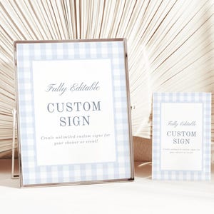 May include: Two framed signs with a light blue gingham border. The larger sign reads "Fully Editable CUSTOM SIGN" and "Create unlimited custom signs for your shower or event!" The smaller sign has the same design and text.