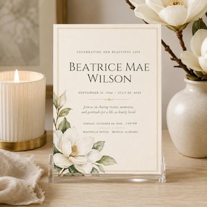 May include: A cream-coloured memorial service announcement card featuring a watercolour magnolia illustration, gold border, and black text reading CELEBRATING HER BEAUTIFUL LIFE, BEATRICE MAE WILSON, SEPTEMBER 21, 1944 - JULY 26, 2026, and event details.