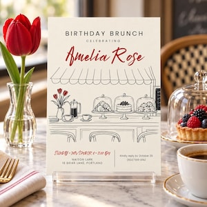 May include: A cream-coloured birthday brunch invitation card featuring a black line drawing of a cafe counter with pastries and coffee. The text reads BIRTHDAY BRUNCH CELEBRATING Amelia Rose, Sunday November 6 11:00 AM, Maison Lark 18 Briar Lane Portland.