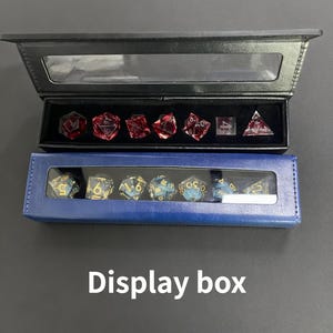 K&ouml;nnte beinhalten: Zwei Pr&auml;sentationsboxen, eine schwarze und eine blaue, die jeweils polyedrische W&uuml;rfel enthalten. Die obere Box enth&auml;lt rote W&uuml;rfel, w&auml;hrend die untere Box blaue und goldene W&uuml;rfel enth&auml;lt. Der Text "Display box" steht darunter.