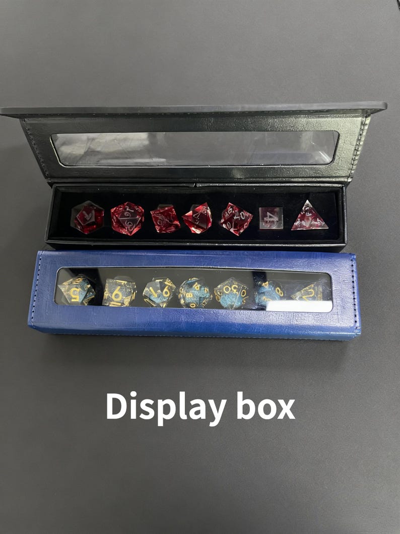 K&ouml;nnte beinhalten: Zwei Pr&auml;sentationsboxen, eine schwarze und eine blaue, die jeweils polyedrische W&uuml;rfel enthalten. Die obere Box enth&auml;lt rote W&uuml;rfel, w&auml;hrend die untere Box blaue und goldene W&uuml;rfel enth&auml;lt. Der Text "Display box" steht darunter.