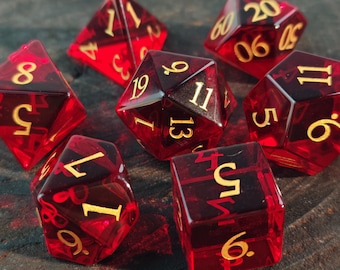 May include: A set of seven translucent red polyhedral dice with gold-coloured numbers. The collection includes a d20, d12, d10, d8, d6, d4, and a percentile die, all featuring sharp edges and clear, legible numerals etched into the deep red resin surfaces.