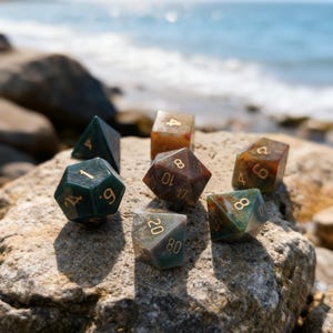 May include: A collection of polyhedral dice in various colors, including green, brown, and clear, with gold numbering. The dice are resting on a rock with the ocean in the background. Ideal for tabletop gaming.
