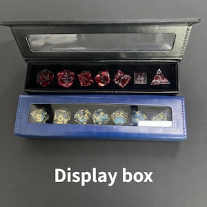May include: Two display boxes, one black and one blue, each containing polyhedral dice. The top box holds red dice, while the bottom box contains blue and gold dice. The text "Display box" is below the boxes.