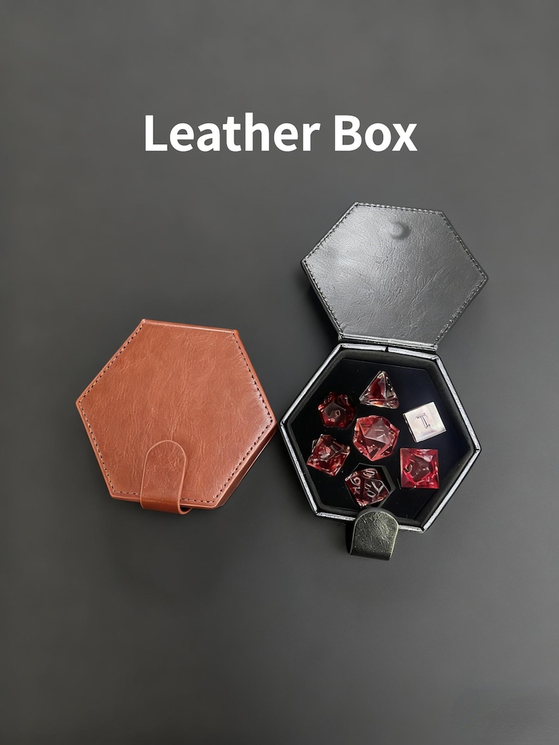 K&ouml;nnte beinhalten: Zwei sechseckige Lederboxen, eine braune und geschlossene, die andere schwarze und offene, mit roten W&uuml;rfeln. Der Text "Leather Box" ist wei&szlig;. Die offene Box enth&auml;lt mehrere rote W&uuml;rfel.