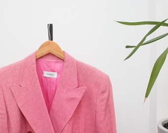 Puede incluir: Un blazer rosa de doble botonadura con solapa de muesca, colgado de una percha de madera. El blazer tiene cuatro botones y un forro rosa. La etiqueta dentro del blazer dice "MISSONI".