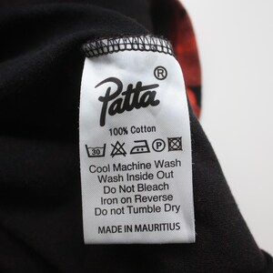 Puede incluir: Primer plano de una prenda negra con una etiqueta blanca. La etiqueta muestra la marca "Patta" e instrucciones de lavado. La tela es 100% algod&oacute;n y est&aacute; hecha en Mauricio.