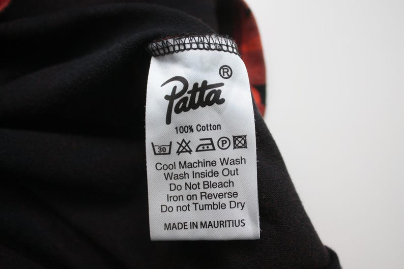Puede incluir: Primer plano de una prenda negra con una etiqueta blanca. La etiqueta muestra la marca "Patta" e instrucciones de lavado. La tela es 100% algod&oacute;n y est&aacute; hecha en Mauricio.