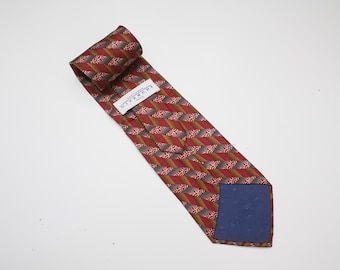 May include: A red, brown, and gold patterned tie with a blue lining. The tie has a repeating geometric design and a label that reads "GIVENCHY PARIS". The tie is on a white background.