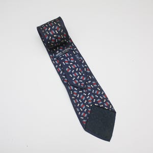 Puede incluir: Una corbata azul marino con un patrón repetitivo de rectángulos rojos, blancos y azules. La corbata está hecha de tela lisa y presenta el texto "mila schon". Un accesorio clásico.
