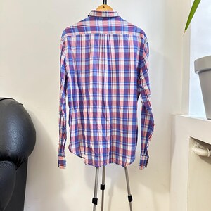 Peut inclure: Chemise &agrave; manches longues &agrave; carreaux bleus, rouges et blancs, pr&eacute;sent&eacute;e sur un support tr&eacute;pied. La chemise a un col boutonn&eacute; et des poignets. Le motif &agrave; carreaux est un design classique. Fabriqu&eacute; en tissu l&eacute;ger.