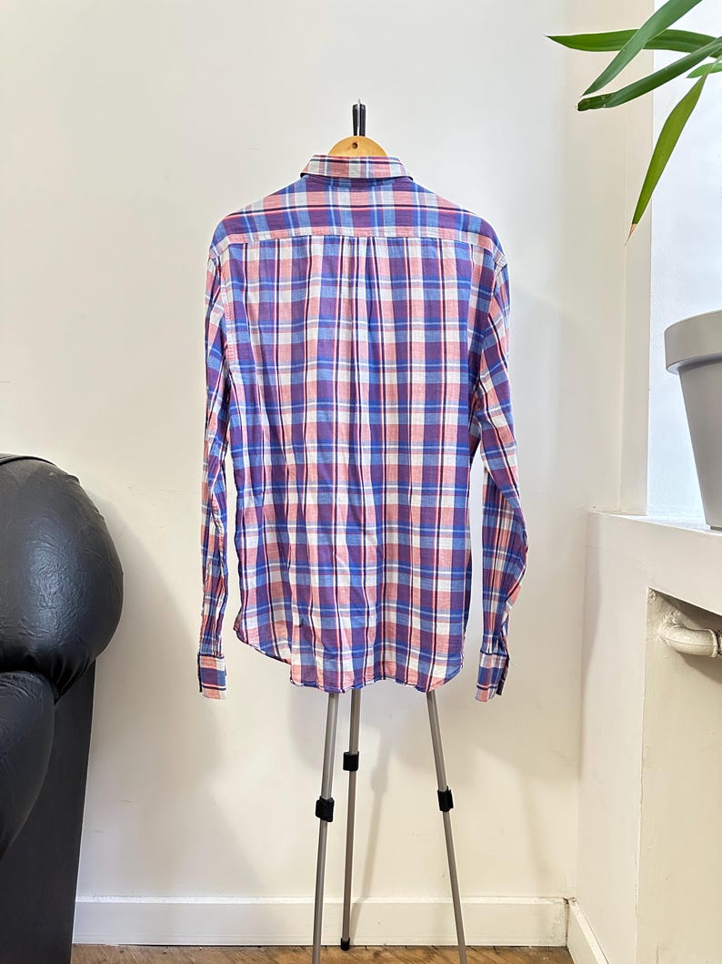 Peut inclure: Chemise &agrave; manches longues &agrave; carreaux bleus, rouges et blancs, pr&eacute;sent&eacute;e sur un support tr&eacute;pied. La chemise a un col boutonn&eacute; et des poignets. Le motif &agrave; carreaux est un design classique. Fabriqu&eacute; en tissu l&eacute;ger.