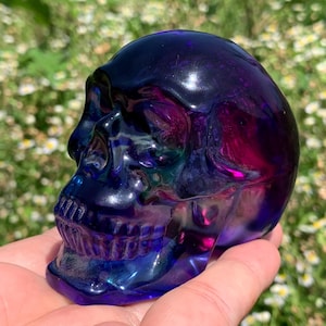 May include: A decorative skull figurine with a glossy finish. The skull is a blend of blue, purple, and pink hues. The product is a unique decorative item.