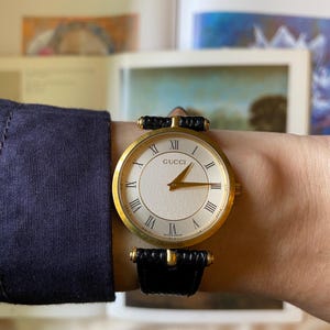 Vintage Gucci Swiss Made-horloge – goudkleurige kast, Romeinse cijfers, witte wijzerplaat met textuur, zwarte leren band – minimalistische unisex stijl