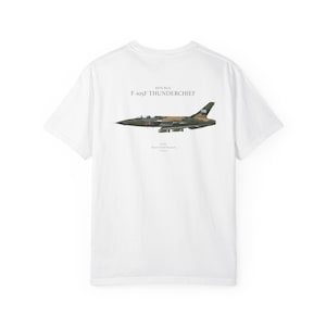 May include: White t-shirt featuring a detailed illustration of a Republic F-105F Thunderchief aircraft in shades of green, brown, and gray. The text "REPUBLIC F-105F THUNDERCHIEF" is printed above the aircraft image.