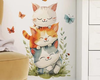 May include: A wall decal featuring three stacked, smiling cartoon cats in shades of white, orange, and gray. Butterflies in orange and blue flutter around the cats, with green foliage at the base. The design is whimsical and suitable for a nursery or child's room.