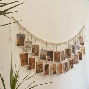 May include: A decorative photo display featuring a string of wooden beads with small wooden clips holding up a series of small rectangular photos. The photos display various images in warm tones, creating a cozy, aesthetic vibe.