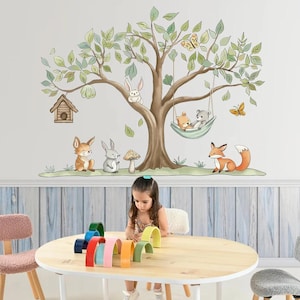 May include: A wall decal depicting a tree with green foliage and various woodland animals, such as a fox, rabbits, and bears. A child is seated at a round wooden table with colourful wooden arches.