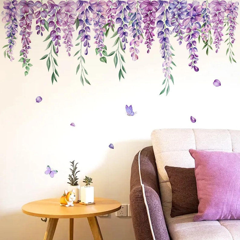 May include: A wall decal featuring cascading purple wisteria flowers and green leaves. The design includes purple butterflies and falling petals. A small wooden table with plants and a dog figurine is in the foreground.