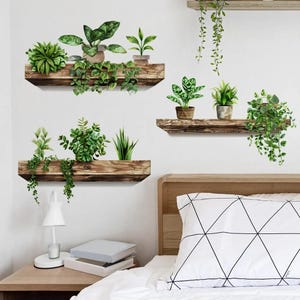May include: Wall decals depicting green plants in pots and hanging from rustic wooden shelves. The image shows a bedroom setting with a bed, nightstand, and a white wall decorated with the plant decals. The decals add a touch of nature to the room, creating a natural aesthetic.