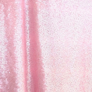 May include: Close-up of a pink sequin fabric. The fabric is a pale pink colour and is covered in small, round sequins that catch the light. The sequins are densely packed together, creating a shimmering effect. The fabric is likely used for clothing or decorative purposes.