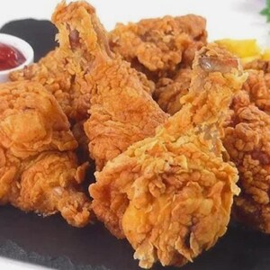May include: A plate of golden-brown fried chicken pieces, including drumsticks and other cuts, with a side of french fries and a small bowl of red ketchup. The chicken has a crispy, textured coating.