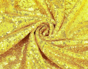 Puede incluir: Primer plano de una tela de lentejuelas de color amarillo dorado. La tela está drapeada y doblada, creando un patrón arremolinado. Las lentejuelas están densamente empaquetadas, reflejando la luz y agregando un efecto brillante. Ideal para manualidades, moda o decoración de eventos.