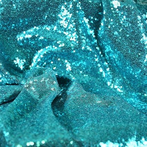May include: Close-up of teal sequin fabric. The fabric is draped and folded, creating shadows and highlights. The sequins are small and round, reflecting light. This fabric is suitable for apparel and decorative projects.