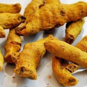 Puede incluir: Primer plano de varias raíces de cúrcuma, mostrando un vibrante color amarillo-naranja. Las raíces tienen una superficie rugosa y texturizada, con formas irregulares. La imagen está bien iluminada, resaltando el color y la textura natural de la cúrcuma.