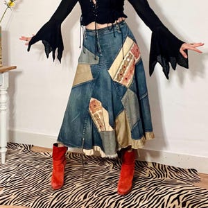 Könnte beinhalten: Ein schwarzes Oberteil mit ausgestellten Ärmeln und Schnürung vorne wird mit einem Patchwork-Jeansrock kombiniert. Der Rock hat verschiedene Stoffflicken. Das Outfit wird durch rote Wildlederstiefel ergänzt.
