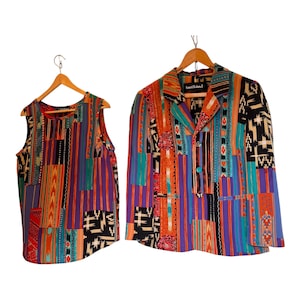 Puede incluir: Un conjunto de top sin mangas y blazer de manga larga con un vibrante patrón de retazos multicolor que incluye rayas, formas geométricas y motivos florales en tonos morado, naranja, azul turquesa, negro y rojo, colgados en perchas de madera.