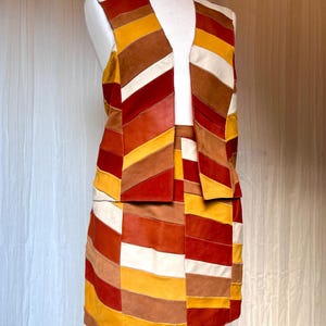 Puede incluir: Un conjunto de chaleco sin mangas y falda a juego confeccionado con paneles de cuero multicolor. La prenda presenta un patrón geométrico de rayas diagonales y verticales en tonos rojo oscuro, amarillo mostaza, bronceado, marrón y blanco roto.
