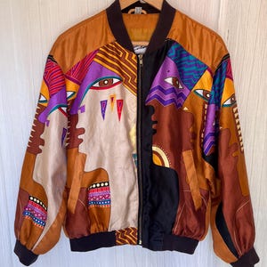 May include: A long-sleeve bomber jacket featuring a vibrant, multi-colored graphic print of abstract faces and geometric patterns. The jacket has a black ribbed collar, cuffs, and hem, a full-length front zipper, and two side pockets in shades of brown.
