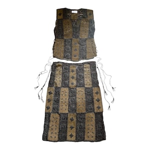 May include: A two-piece outfit comprising a vest and a skirt. The vest and skirt are constructed with a patchwork design, alternating tan suede squares and dark grey, open-weave fabric. The skirt has drawstrings.