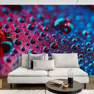 May include: Abstract wall mural featuring a macro shot of water droplets in shades of red and blue. The droplets are in focus, creating a textured, three-dimensional effect. The mural is installed behind a white sofa with decorative pillows.