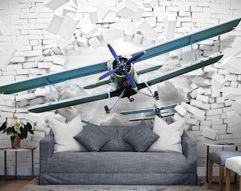 May include: A mural depicting a biplane bursting through a white brick wall. The biplane is light blue with a dark blue propeller and is set against a cloudy sky. The wall is breaking apart.