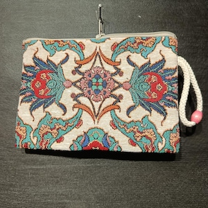 Bolso de gobelino hecho a mano con intrincado patrón floral otomano en rojo, verde azulado y azul; incluye correa de muñeca de cordón blanco y cuenta rosa.