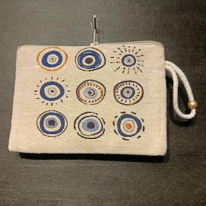 Bolso de mano Gobelino con ojo turco, hecho a mano, con fondo beige neutro.