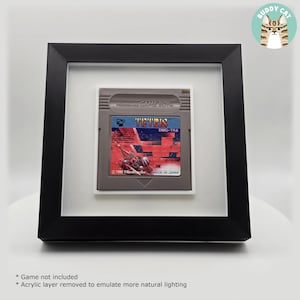 以下が含まれることがあります： 額装されたビンテージテトリスゲームボーイカートリッジ。グレーのカートリッジには、テトリスのロゴとゲームグラフィックが描かれたカラフルなラベルが付いています。白いマットが付いた黒いフレームは、すっきりとした印象を与えます。ゲームカートリッジは1989年製です。