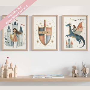 May include: Set of three framed art prints with a fairytale theme. The prints feature illustrations of a castle, a knight with a shield, and a girl riding a dragon. The frames are light wood, and the artwork has a soft, watercolor style.