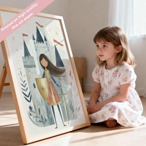May include: A framed print featuring a medieval illustration of a female knight with a sword and shield in front of a castle. The print is in a light wooden frame. The text "Printed on high quality, fine art paper" is visible. The print is displayed on a wooden easel.