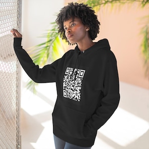 May include: Black hoodie featuring a large white QR code. The hoodie has a front pocket and a drawstring hood. The person in the image is wearing the hoodie.