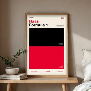 May include: A framed poster with the text "Haas Formula 1" in a bold font. The poster features a black and red color block design with the American flag in the upper right corner. Additional text includes "VF-25", "Ferrari", and "2016".